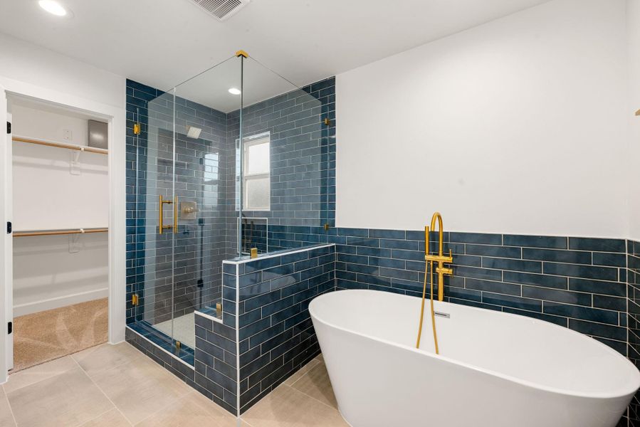 Stunning primary bathroom featuring a freestanding soaking tub with gold fixtures and a glass-enclosed walk-in shower. Beautiful blue tile surrounds add character and contrast, creating a spa-inspired retreat with a modern, upscale feel.