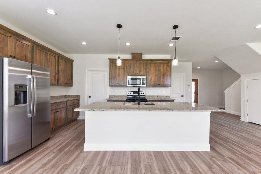 Kitchen with light wood finished floors, a sink, a center island with sink, visible vents, and appliances with stainless steel finishes