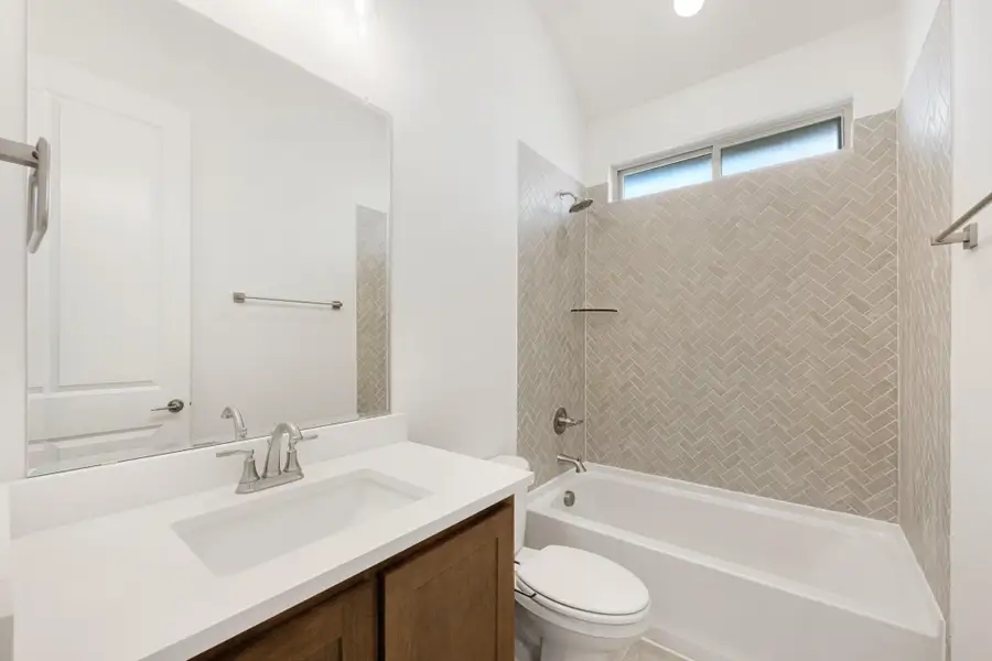Bathroom with wood vanity, white countertop, and tub-shower combo with herringbone tile surround Bathroom with wood vanity, white countertop, and tub-shower combo with herringbone tile surround