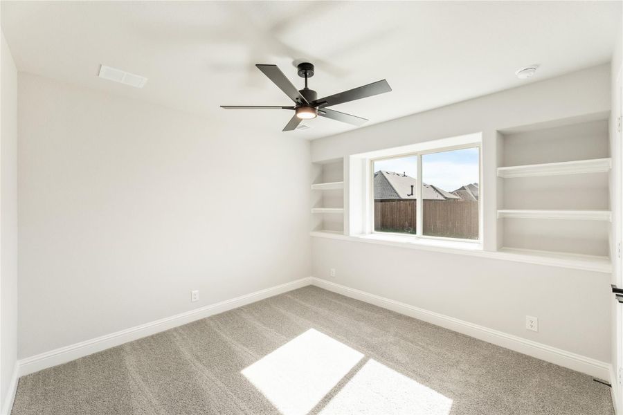 Empty bedroom with carpet, ceiling fan, and built-in shelves beside a window