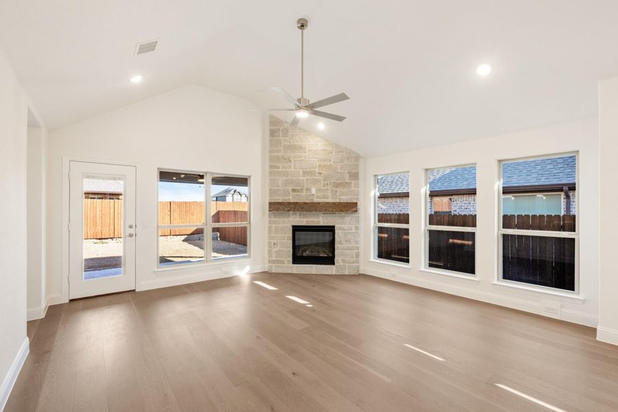 Open living room with vaulted ceiling, stone fireplace, ceiling fan, and hardwood floors Open living room with vaulted ceiling, stone fireplace, ceiling fan, and hardwood floors