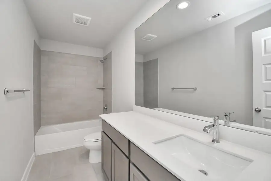 Secondary bath features tile flooring, bath/shower combo with tile surround, light stained wood cabinets, beautiful light countertop. Sample photo of completed home with similar floor plan. Actual colors and selections may vary.