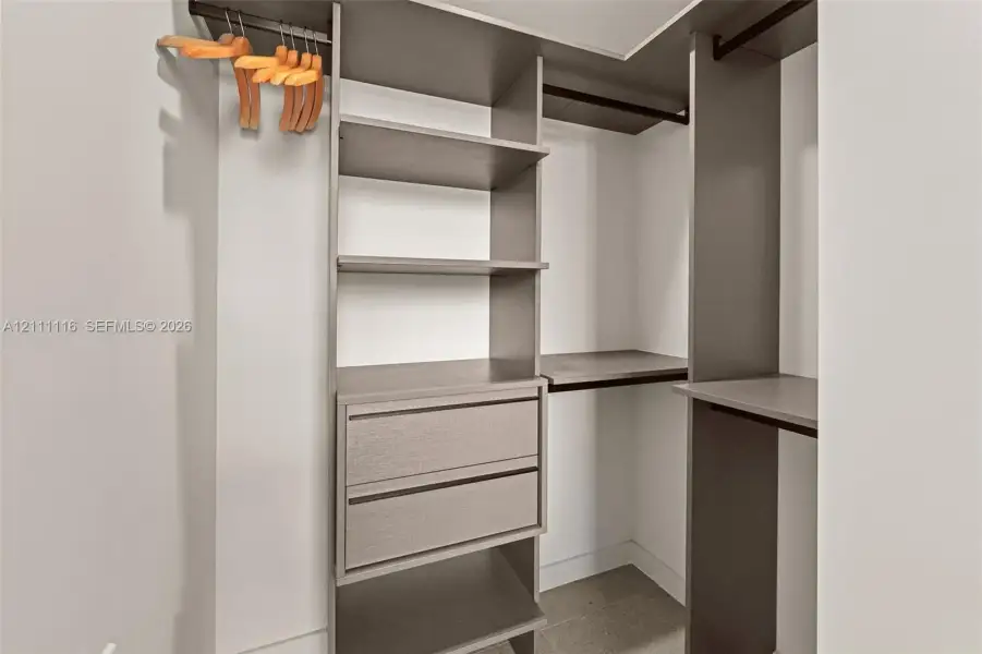 Walk-in closet featuring floor-to-ceiling custom cabinetry, adjustable shelving, integrated storage drawers, and dual hanging rods
