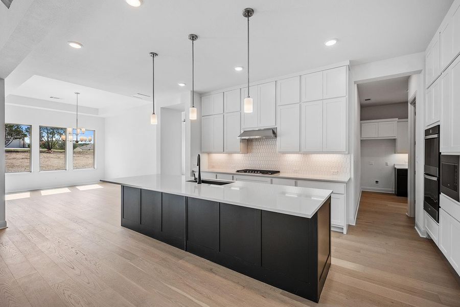Kitchen featuring an island with sink, decorative light fixtures, backsplash, white cabinetry, and recessed lighting