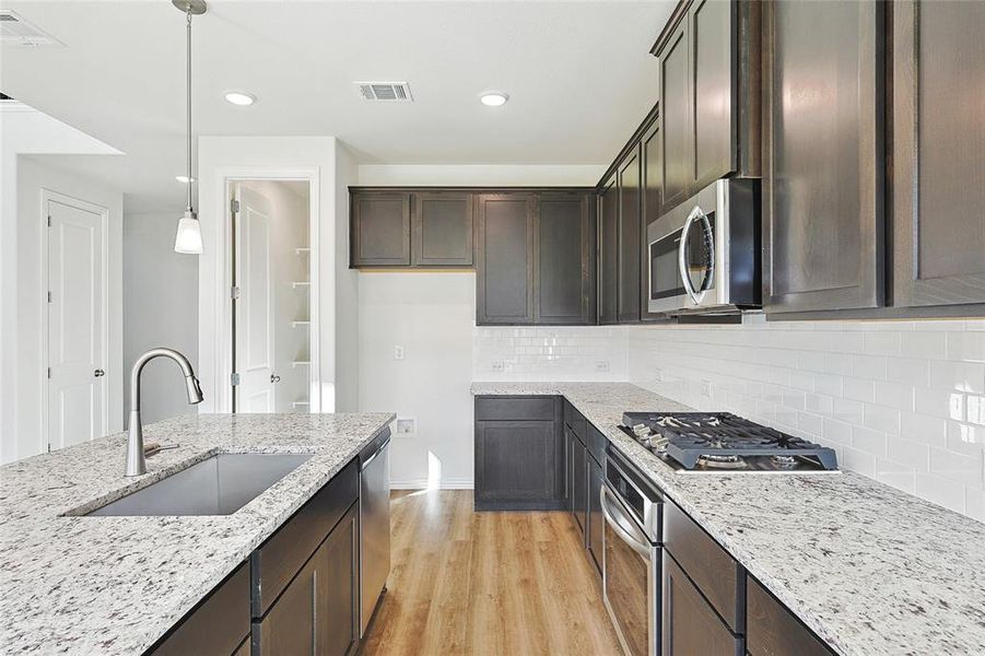 Kitchen with tasteful backsplash, light wood-type flooring, appliances with stainless steel finishes, sink, and pendant lighting