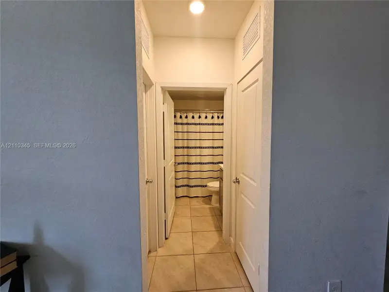 Hallway featuring tile flooring, neutral wall paint, and multiple interior doors with polished metal hardware
