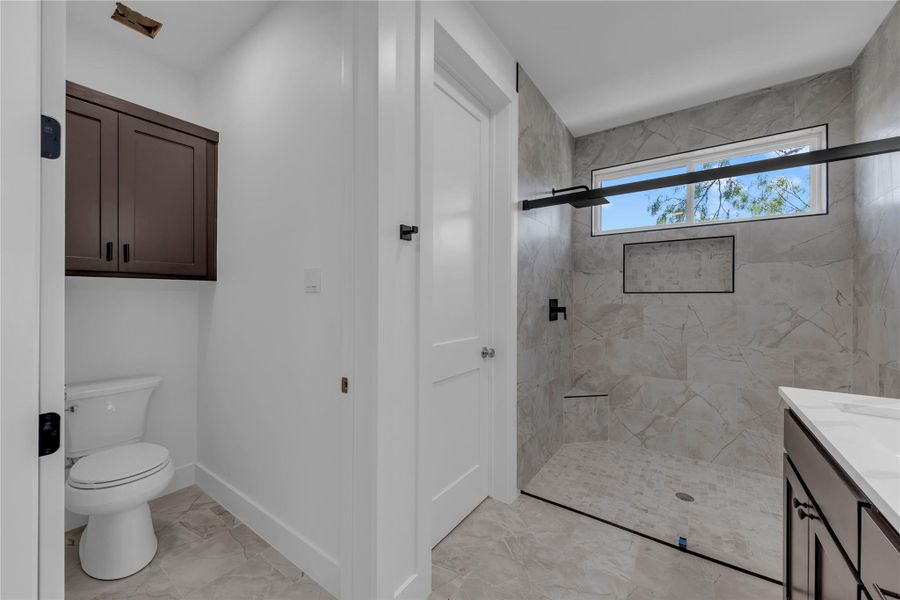 A walk-in tile shower sits adjacent to a private water closet with built-in cabinetry.