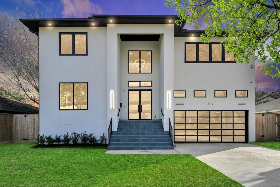 A closer look at the grand front elevation highlights the soaring two-story entry, sleek glass-paneled garage door, and sophisticated exterior lighting that elevates the home’s modern design.