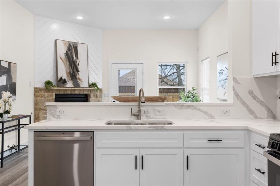 Kitchen with dishwasher, white cabinets, sink, light wood-type flooring, and light stone counters