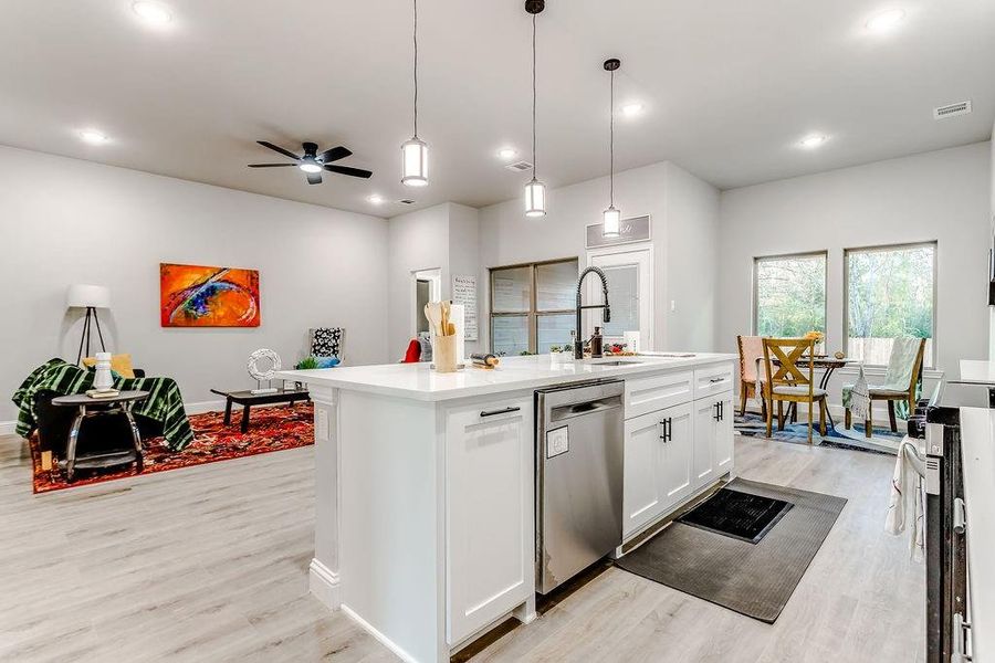 Kitchen featuring light wood-type flooring, white cabinets, a center island with sink, dishwasher, and hanging light fixtures