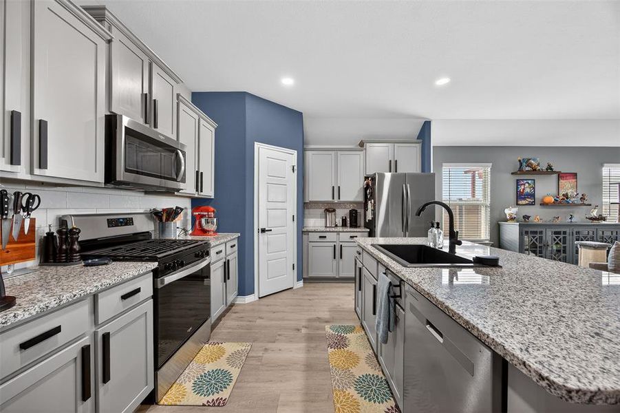 Kitchen with stainless steel appliances, a kitchen island with sink, light stone countertops, light wood-style flooring, and recessed lighting