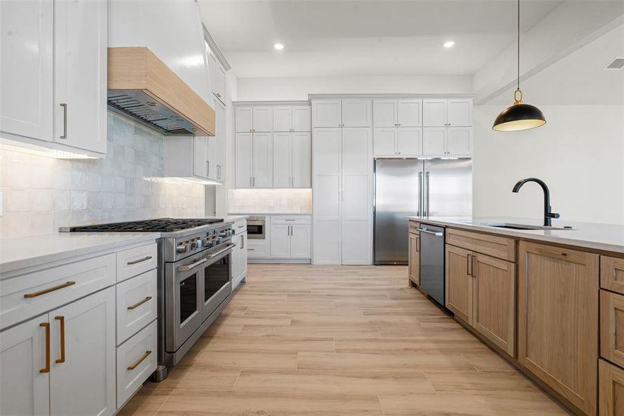 Kitchen featuring white cabinetry, appliances with stainless steel finishes, backsplash, hanging light fixtures, and premium range hood Kitchen featuring white cabinetry, appliances with stainless steel finishes, backsplash, hanging light fixtures, and premium range hood