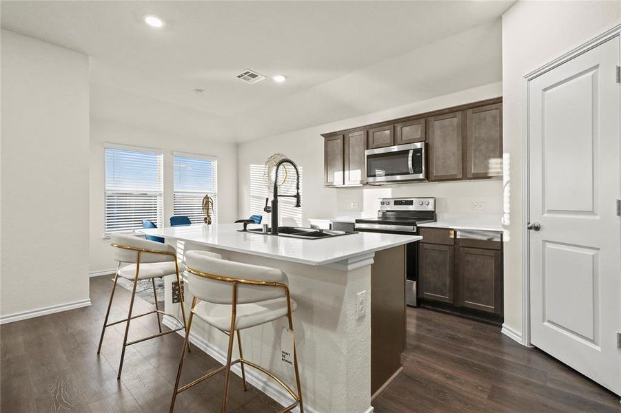 Kitchen featuring an island with high-end brown cabinets, appliances with stainless steel finishes, and  wood-style flooring