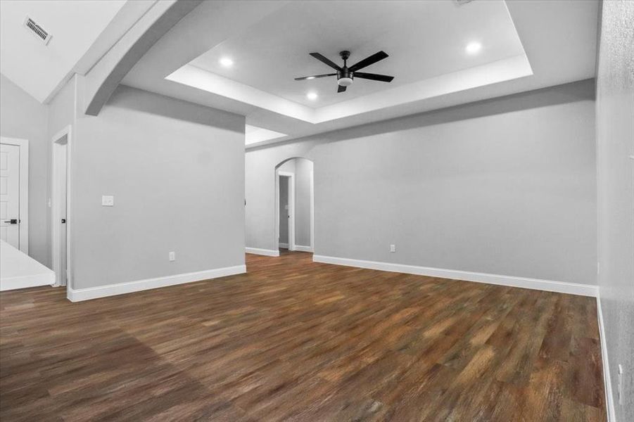 Unfurnished living room featuring dark hardwood / wood-style floors, ceiling fan, and a raised ceiling