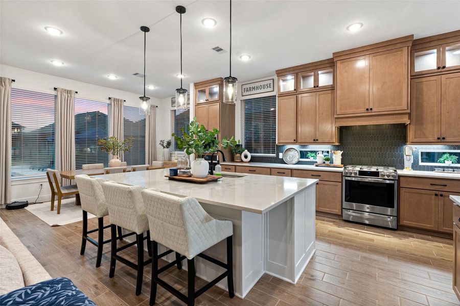 The soaring family room features high ceilings with beams, an electric fireplace wall, and flows into a chef's kitchen with quartz countertops, oversized island, luxe pantry, Barley cabinetry with glass uppers, and GE Profile appliances including double ovens with built-in air fryer. The soaring family room features high ceilings with beams, an electric fireplace wall, and flows into a chef's kitchen with quartz countertops, oversized island, luxe pantry, Barley cabinetry with glass uppers, and GE Profile appliances including double ovens with built-in air fryer.