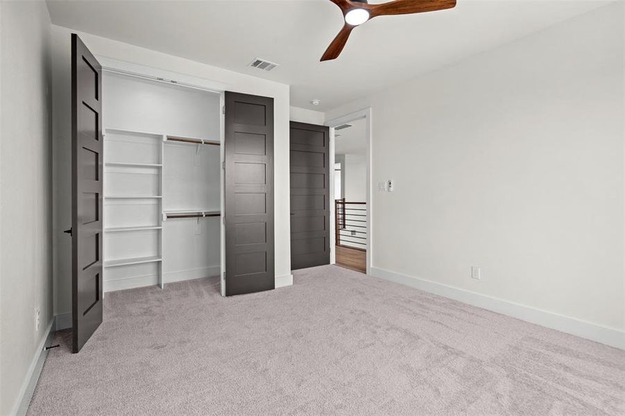 This room features light-colored carpet flooring, a modern ceiling fan with wooden blades, and white walls This room features light-colored carpet flooring, a modern ceiling fan with wooden blades, and white walls