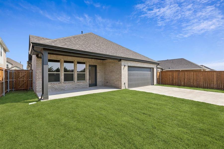 Rear view of house with brick siding, roof with shingles, driveway, a patio, and a garage