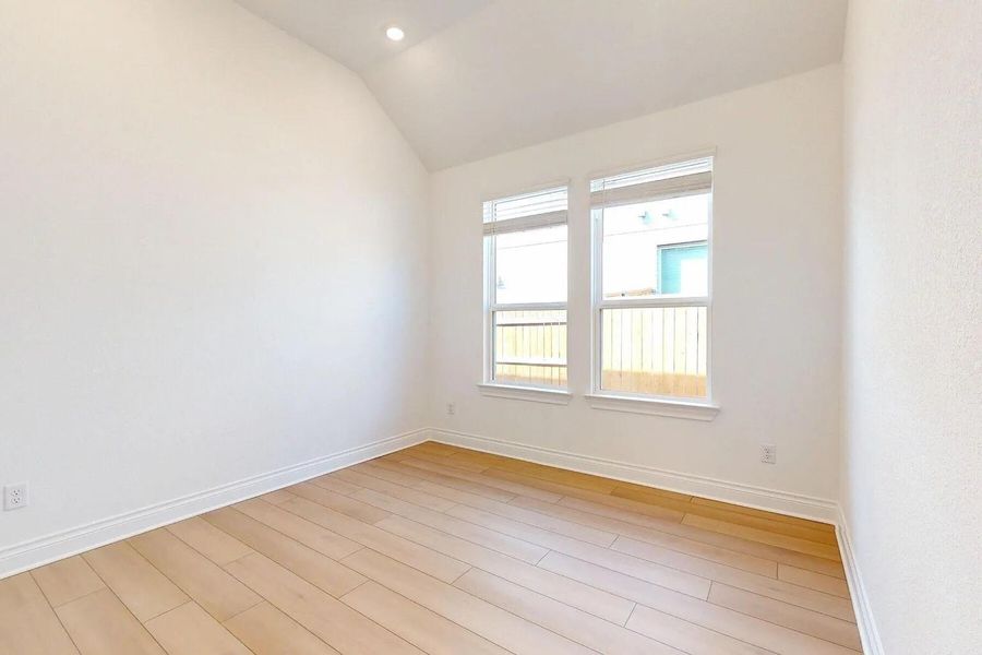 This room features light hardwood flooring, white walls, and a vaulted ceiling with recessed lighting