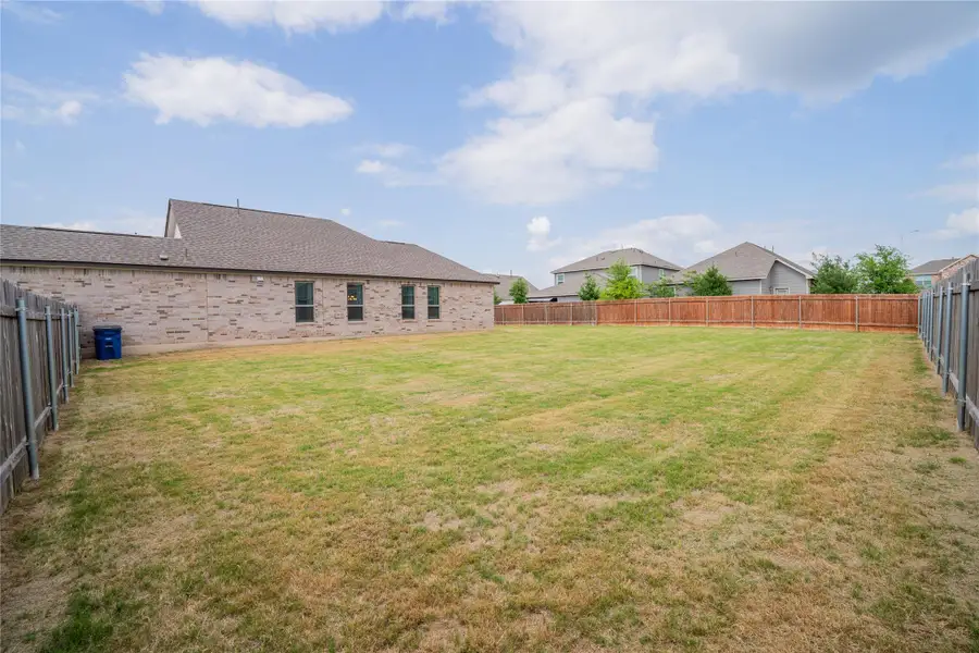 Expansive backyard featuring a large green space, privacy fencing, and a brick exterior with multiple windows Expansive backyard featuring a large green space, privacy fencing, and a brick exterior with multiple windows