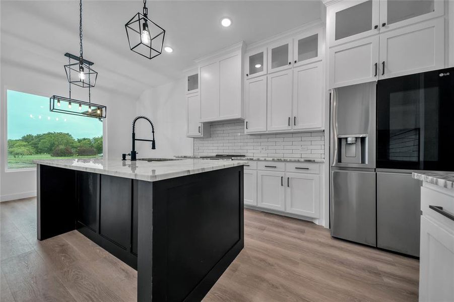 Kitchen featuring white cabinets, pendant lighting, a center island with sink, and sink