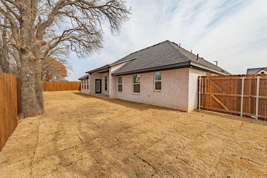 Rear view of house with roof with shingles, brick siding, a fenced backyard, a gate, and a patio area