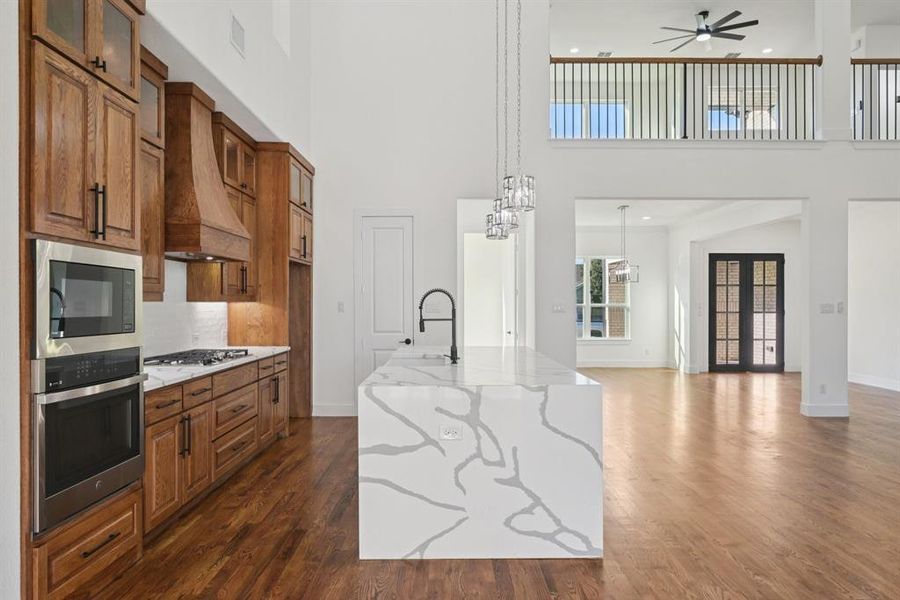 Kitchen featuring stained brown cabinets, light stone countertops, open floor plan, stainless steel appliances, and a kitchen island with sink