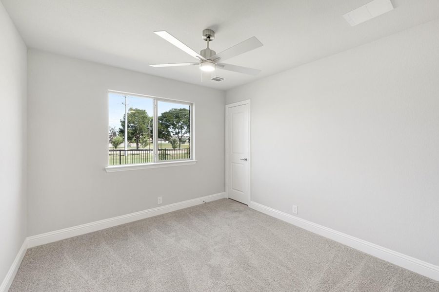 Empty bedroom with gray carpet, ceiling fan, white walls, and a window with outdoor views