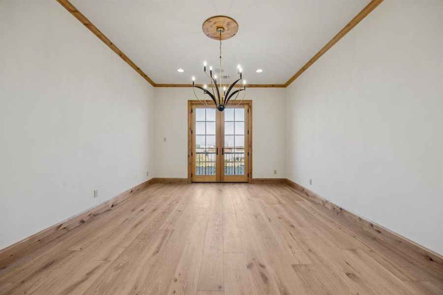 Spare room featuring french doors, light wood-type flooring, recessed lighting, a chandelier, and crown molding