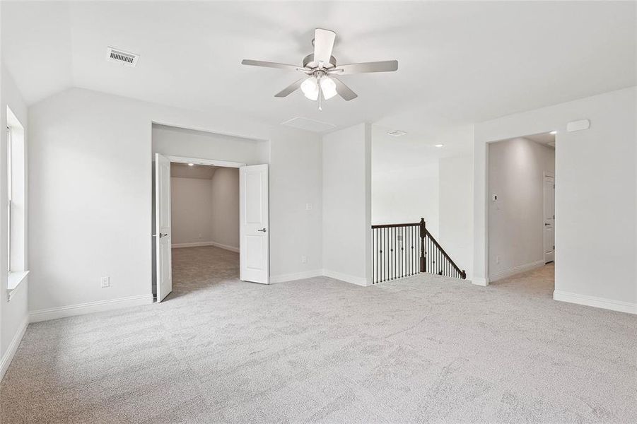 Empty room with ceiling fan, vaulted ceiling, and light colored carpet