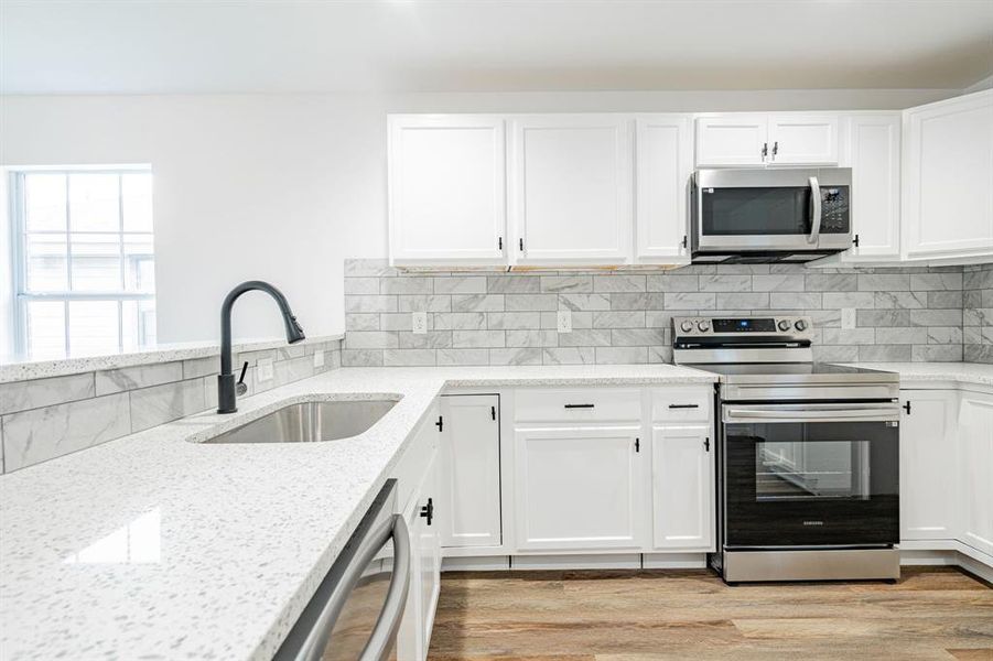 Kitchen with light hardwood / wood-style floors, appliances with stainless steel finishes, decorative backsplash, and sink