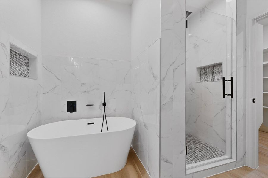 Freestanding soaking tub with matte black fixtures, complemented by a glass-enclosed shower featuring a tiled niche and mosaic floor Freestanding soaking tub with matte black fixtures, complemented by a glass-enclosed shower featuring a tiled niche and mosaic floor