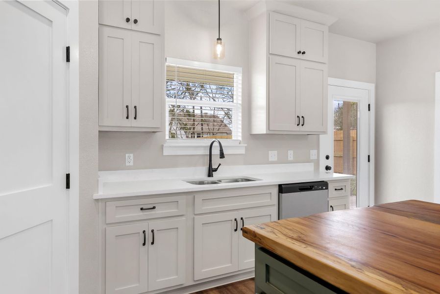 Kitchen featuring wood counters, healthy amount of natural light, stainless steel dishwasher, pendant lighting, and two tone cabinetry