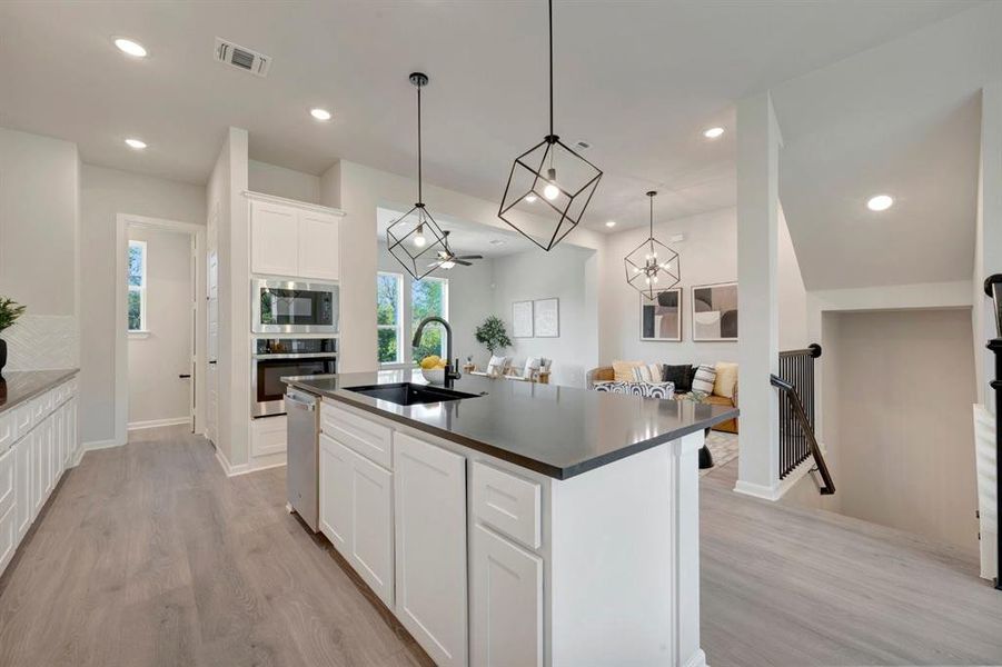Modern kitchen with an island featuring a black sink and faucet, white cabinetry, integrated stainless steel appliances, recessed lighting, and wood-finish flooring