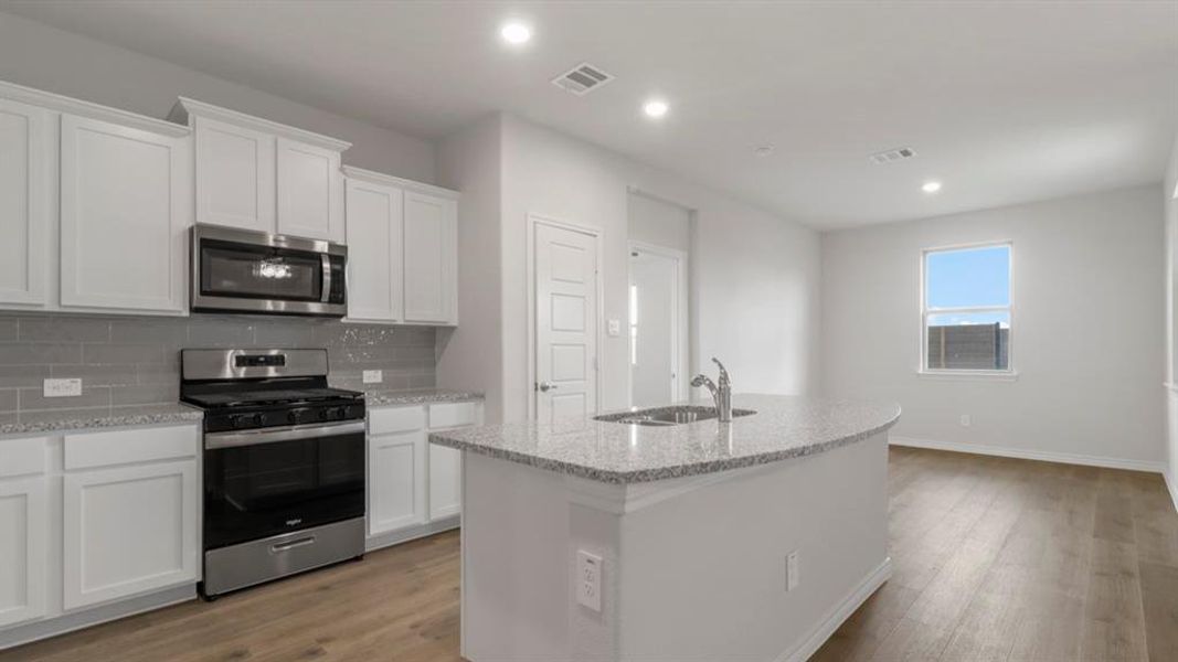 Kitchen with stainless steel appliances, an island with sink, light wood-style flooring, light stone counters, and recessed lighting