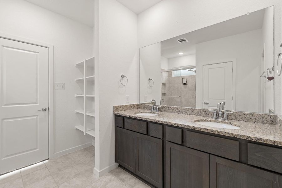 The primary bathroom features a large vanity, featuring dual sinks, wood cabinets, a large mirror, and granite countertops! There's built-in shelving for additional storage.