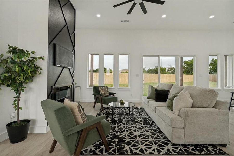 Spacious living area featuring a geometric accent wall with integrated fireplace, light wood-finish flooring, recessed lighting, and a ceiling fan Spacious living area featuring a geometric accent wall with integrated fireplace, light wood-finish flooring, recessed lighting, and a ceiling fan