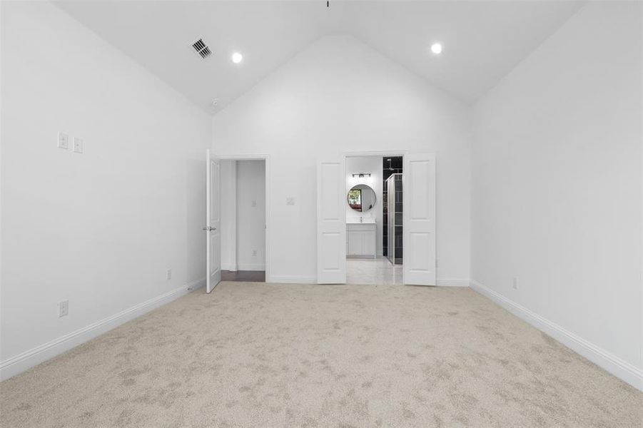 Unfurnished bedroom with ensuite bath, high vaulted ceiling, and light colored carpet