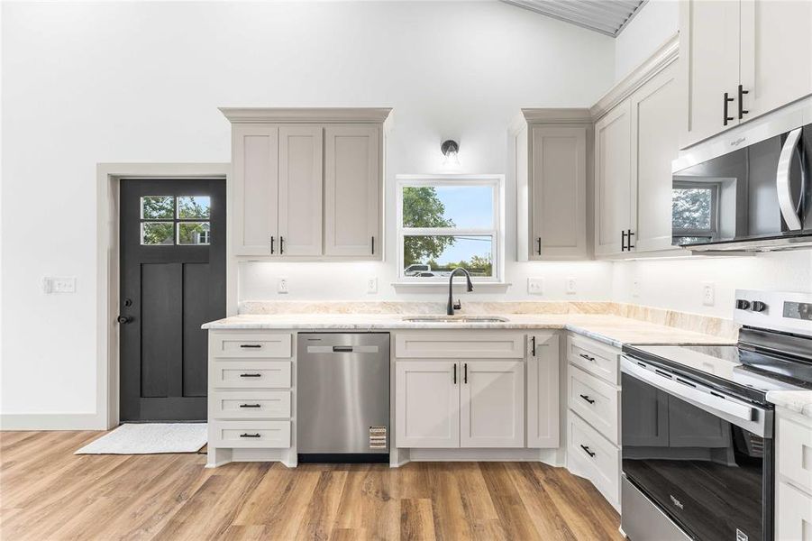 Kitchen featuring appliances with stainless steel finishes, light wood finished floors, light stone countertops, and white cabinets Kitchen featuring appliances with stainless steel finishes, light wood finished floors, light stone countertops, and white cabinets