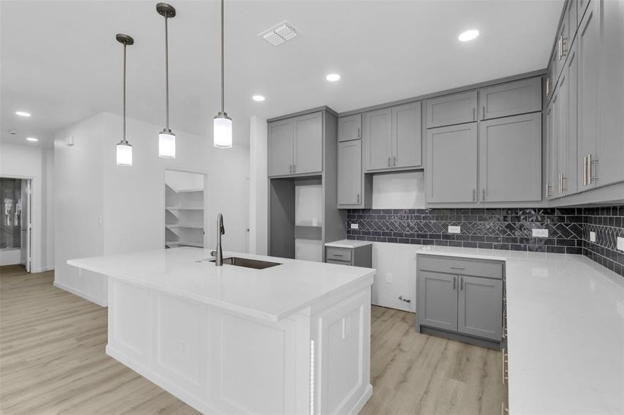 Kitchen featuring gray cabinetry, light stone countertops, a kitchen island with sink, recessed lighting, and light wood-type flooring