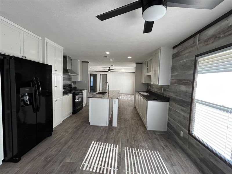 Kitchen with black appliances, wooden walls, dark wood-type flooring, and white cabinetry