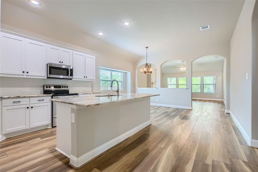 Kitchen featuring stainless steel appliances, decorative light fixtures, light hardwood / wood-style flooring, sink, and a center island with sink