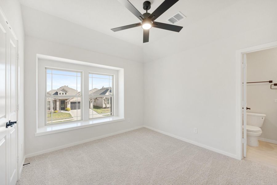 Empty bedroom with carpet, ceiling fan, large window, and ensuite bathroom doorway Empty bedroom with carpet, ceiling fan, large window, and ensuite bathroom doorway