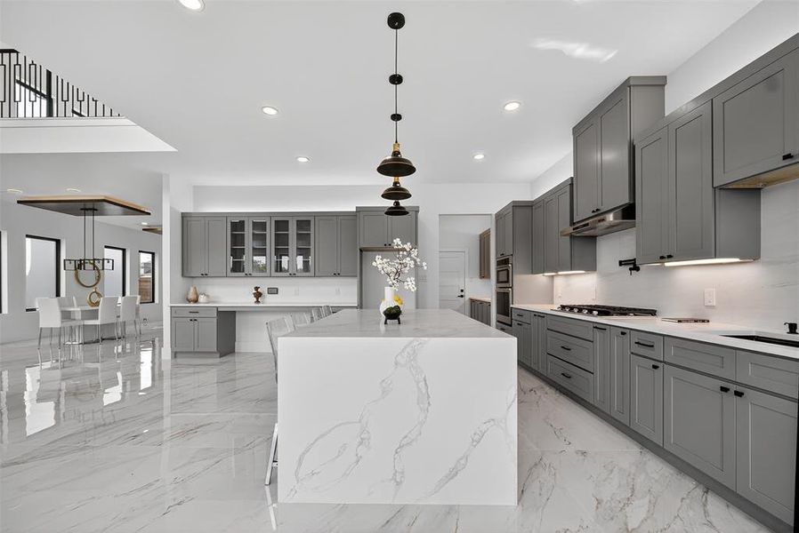 Kitchen with gray cabinetry, a center island, hanging light fixtures, light stone counters, and recessed lighting