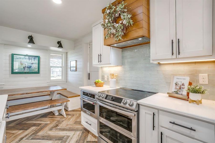 Kitchen featuring stainless steel appliances, white cabinets, parquet flooring, and tasteful backsplash