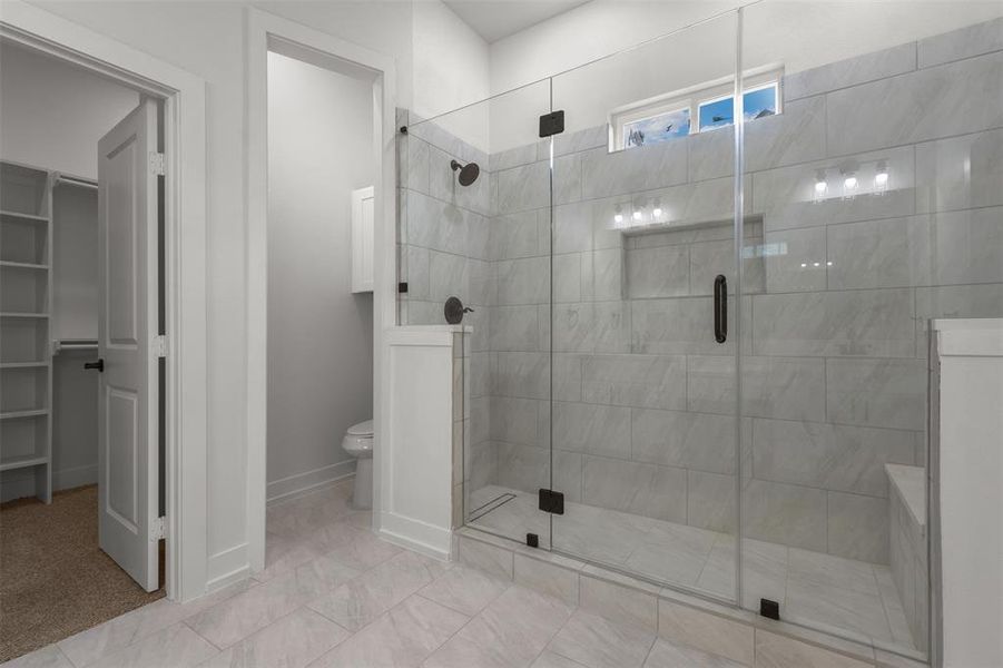 The bathroom features a spacious glass-enclosed shower with light-colored tile walls and a built-in bench