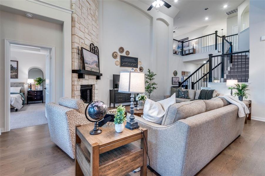 Living area featuring a stone fireplace, wood finished floors, a high ceiling, stairs, and a ceiling fan