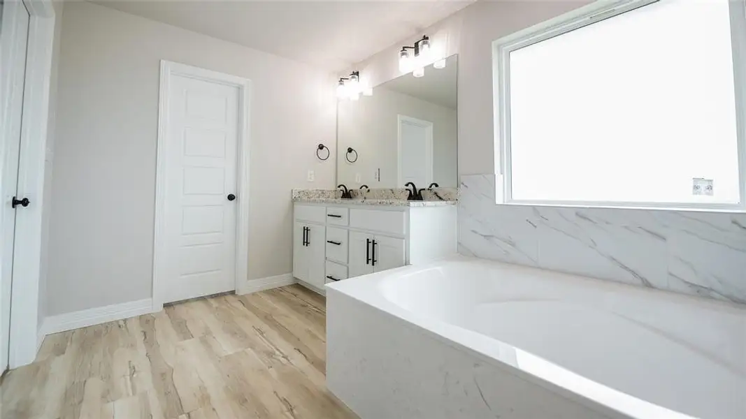 Bathroom featuring double vanity, a garden tub, and wood finished floors Bathroom featuring double vanity, a garden tub, and wood finished floors