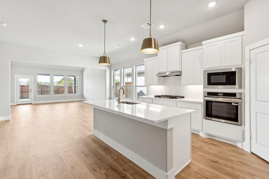 Kitchen with white cabinets, hanging light fixtures, stainless steel appliances, recessed lighting, and an island with sink