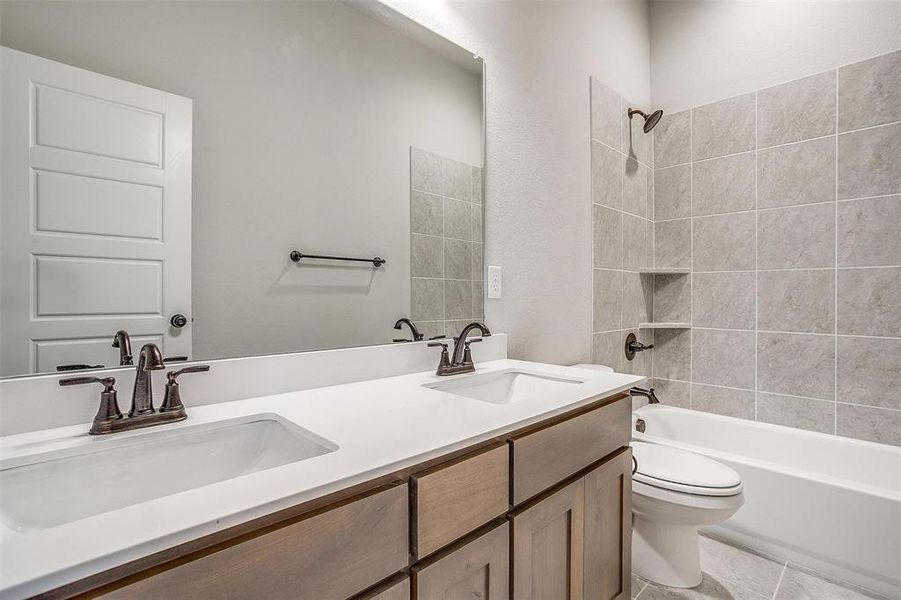 Full bathroom with dual vanity, tile patterned floors, toilet, and tiled shower / bath