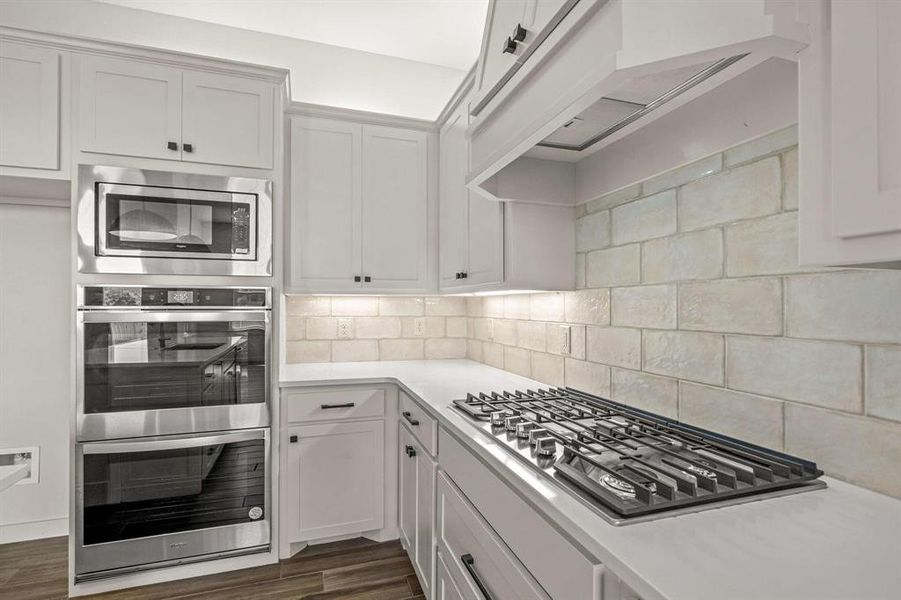 Kitchen with appliances with stainless steel finishes, light countertops, tasteful backsplash, under cabinet range hood, and dark wood-style flooring